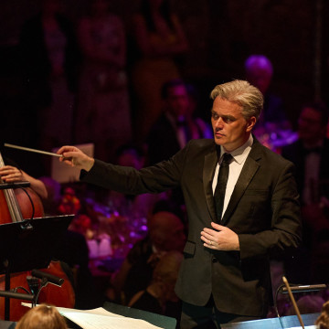 Photo of Ed Gardner in a black suit and tie conducting an orchestra