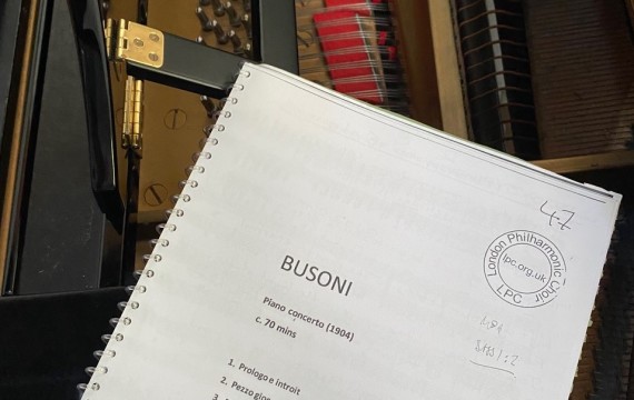 Image shows a score for Busoni's Piano Concerto resting on top of a black grand piano