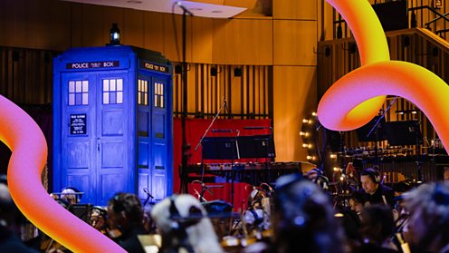 Image shows a picture of the TARDIS from Doctor Who in a recording studio surrounded by musicians