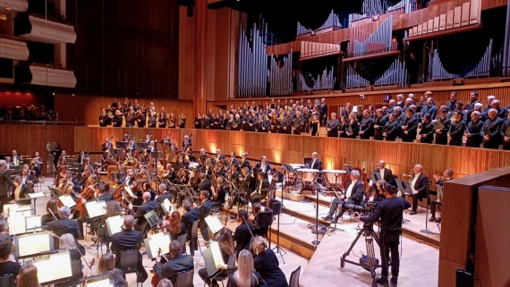 Image shows a large orchestra and choir performing on stage