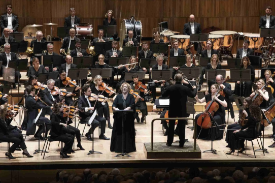 Image is of a large orchestra with solo singer and conductor